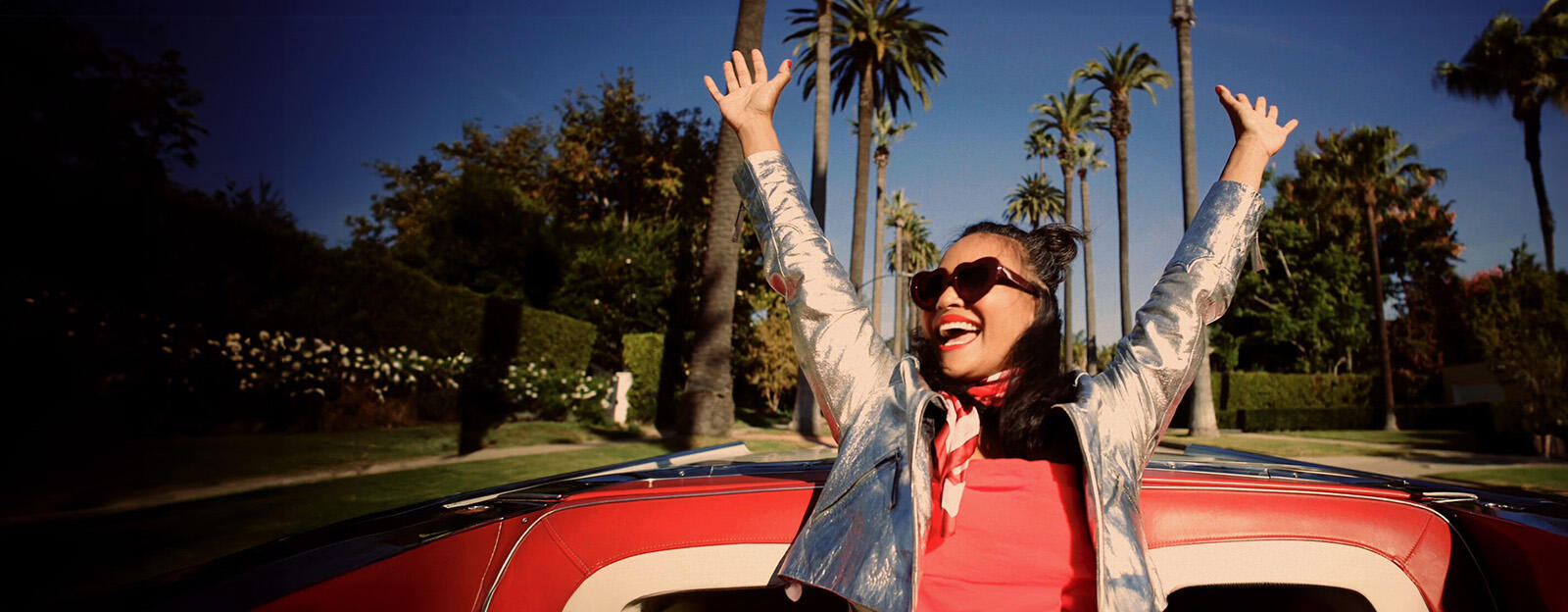 Lady with arms up in the back of a convertible car