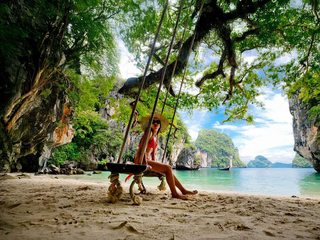 A woman sits on a tree swing on a beach in Phuket