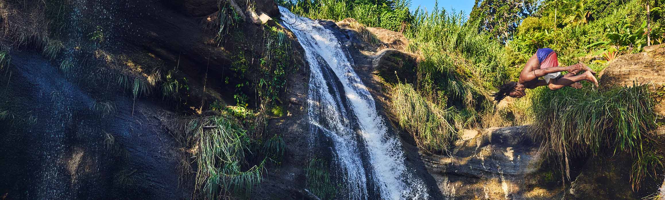 A man somersaults into water with a waterfall in the background