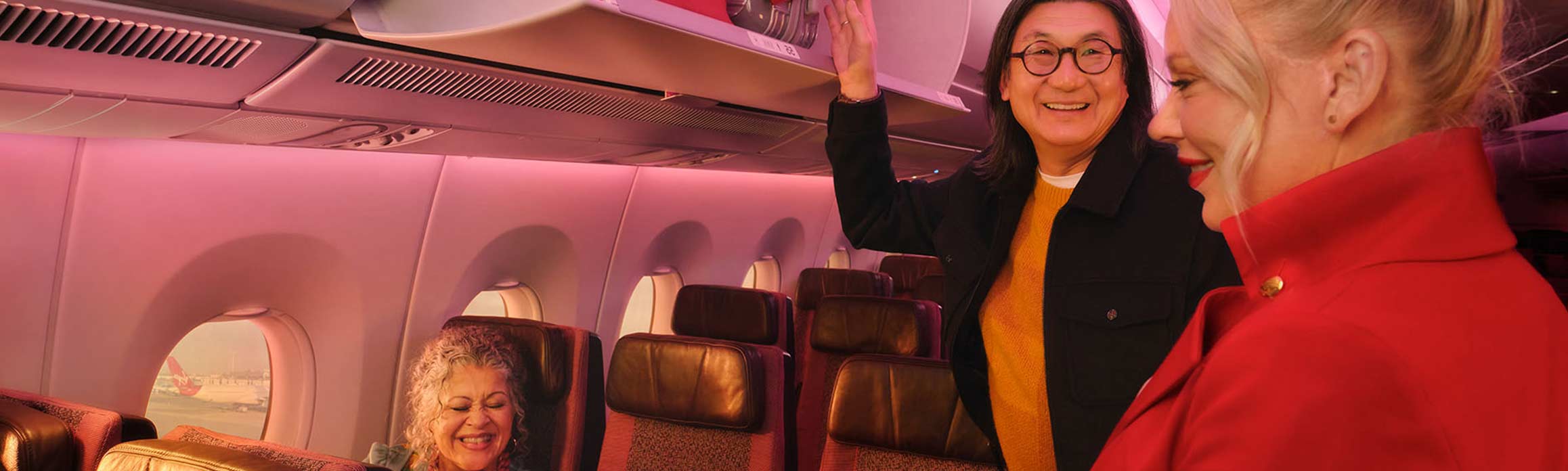 Flight attendant in red jacket talking to customers using overhead locker