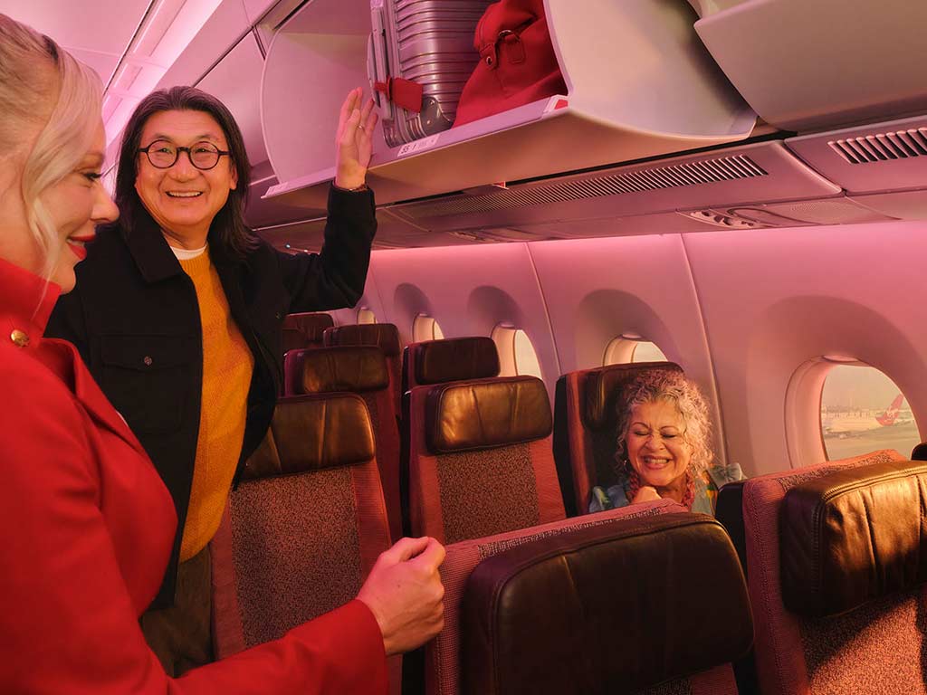 Flight attendant in red jacket talking to customers using overhead locker