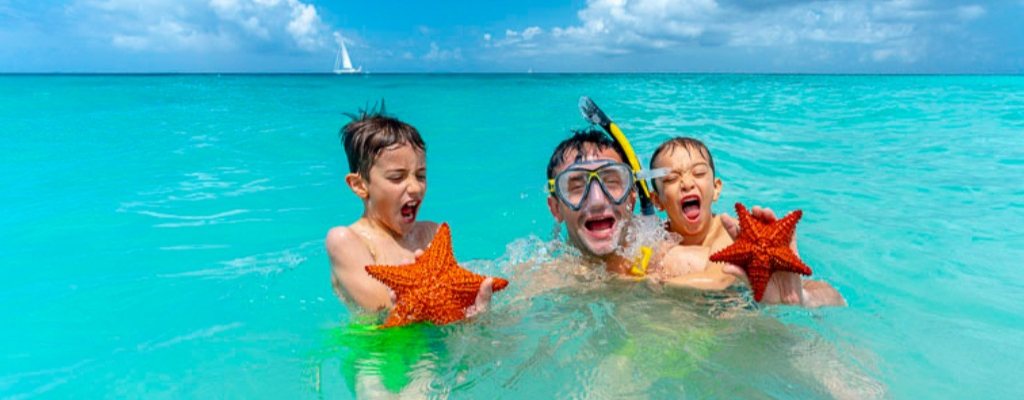 Father and two children snorkelling and holding starfishes in the sea