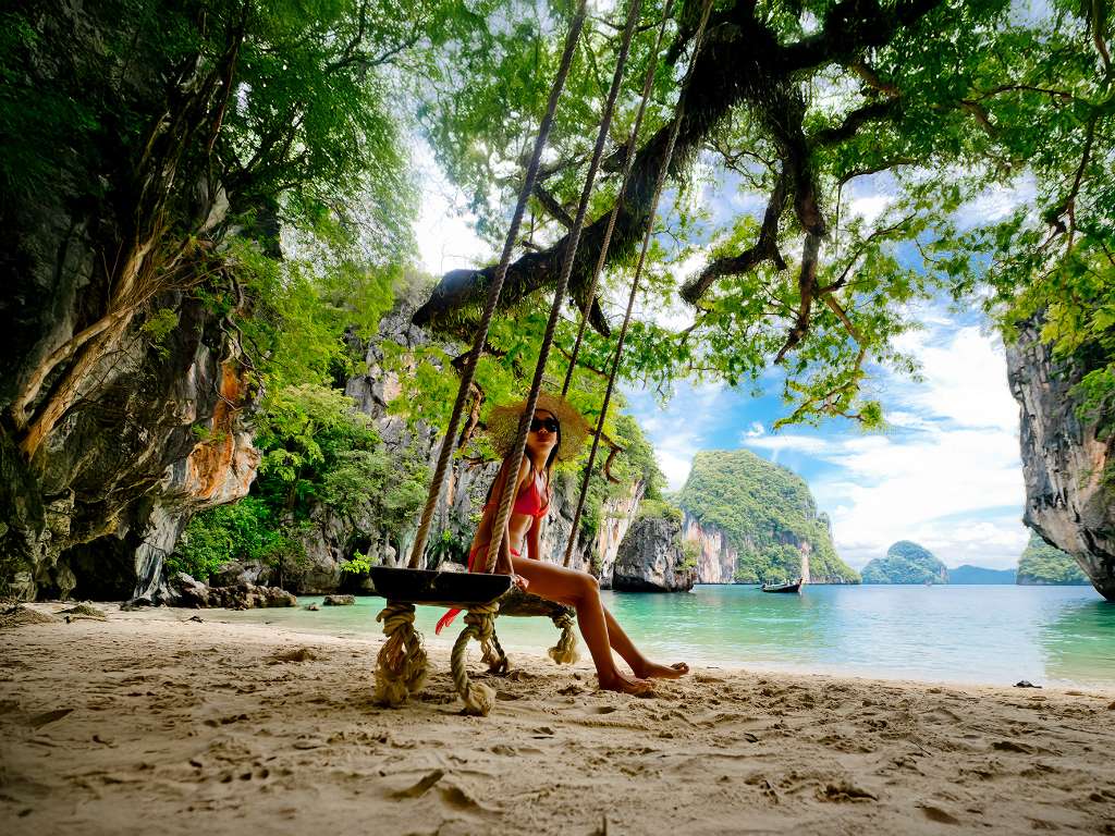 A woman sits on a tree swing on a beach in Phuket